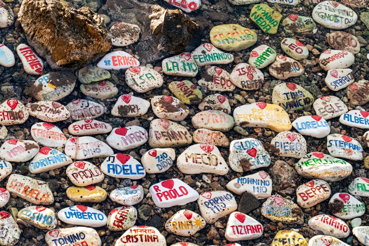 services-02 Vibrant stones with names painted, submerged in a shallow coastal waterway in Italy.