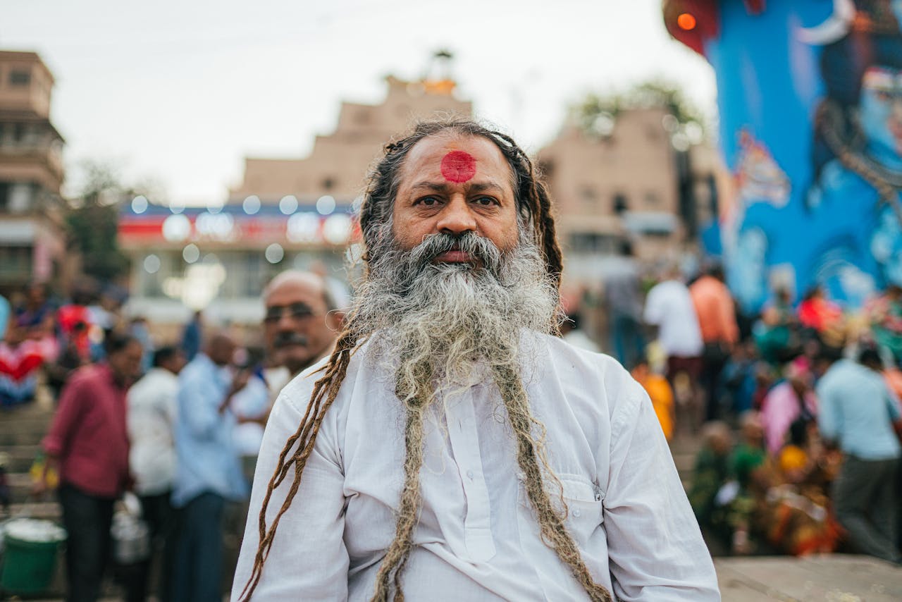 services-03 An elderly man with a red tilak standing in a busy street in Varanasi, India.